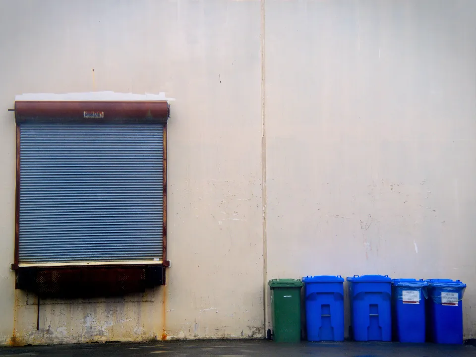 Row of recycling bins lined up against a warehouse wall
